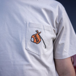 White t-shirt with a small orange and black design on the chest pocket against a dark background