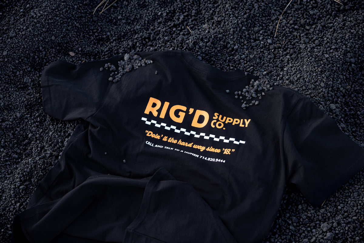 Black jacket with 'Rig'd Supply Co.' logo on a dark textured surface